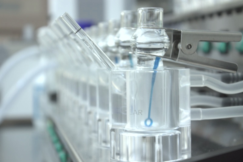 A line of plastic bottles on a conveyor belt in a topical drug product manufacturing facility.