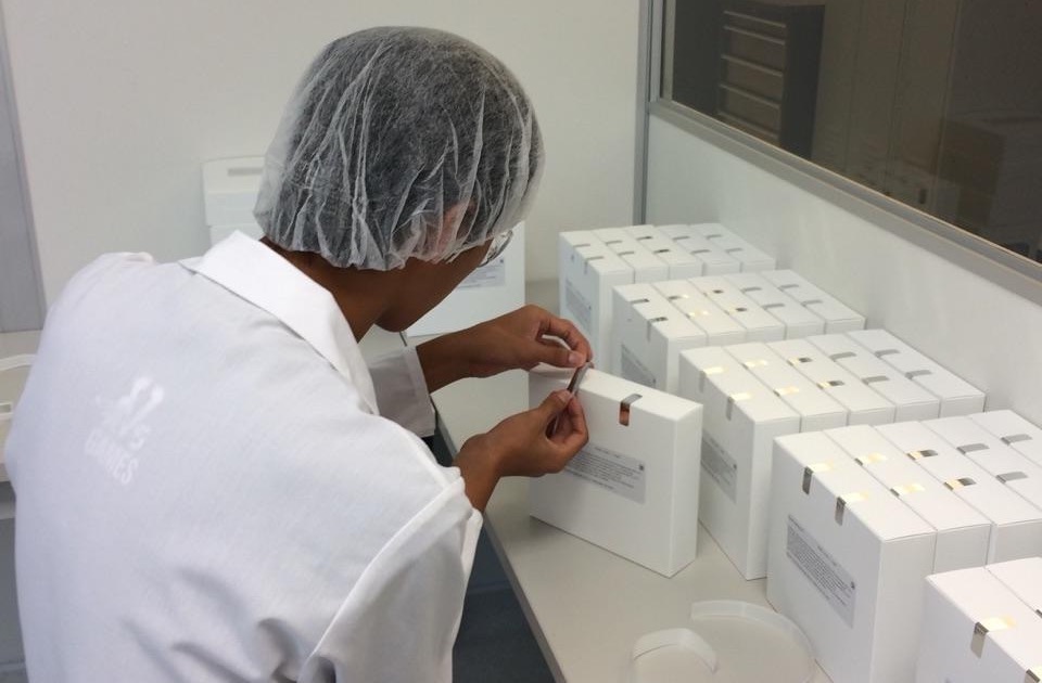 A man in a white lab coat is engaged in topical drug product manufacturing by putting boxes on a table.