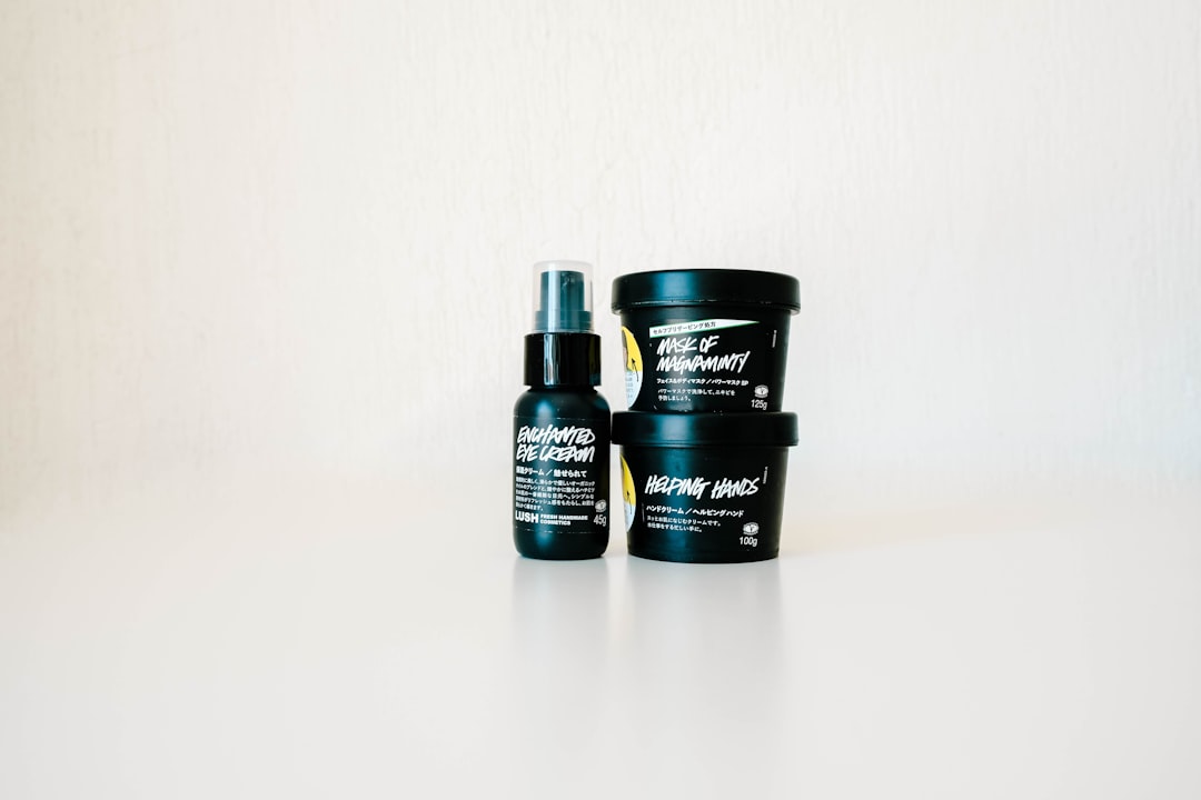 Three black cosmetic containers with white text labels, designed for success in topical product development, sit on a white surface against a plain light background. One is a spray bottle; the other two are round jars.