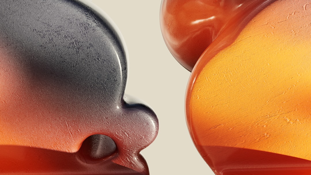 dowdevelopmentlabs6 Close-up of two abstract, rounded objects with smooth textures; reminiscent of creams or gels, one is metallic gray and orange, the other translucent orange with light reflecting off both shapes against a beige background.