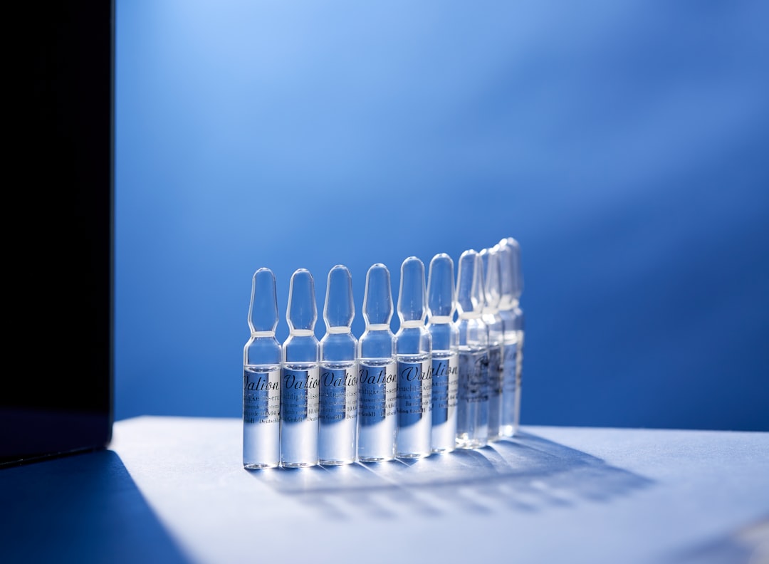 A row of nine clear glass ampoules filled with liquid, arranged upright on a white and blue surface with a blue background, highlights the precision often required in ophthalmic formulation development.