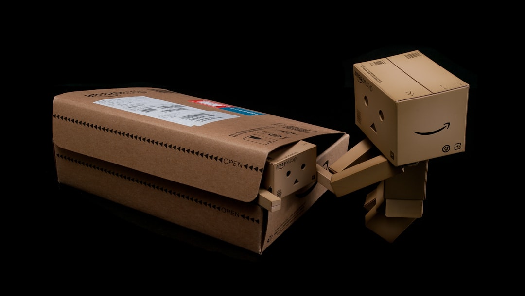 Two cardboard box figurines, one emerging from a shipping envelope and another helping, evoke themes of pharmaceutical packaging and packaging compatibility testing against a black background.